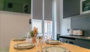 A dining table set with plates, glasses, and cutlery, with a kitchen area visible in the background. - 3bdr/6p Flat- Villemomble- 20min From Paris by RER (Villemomble)