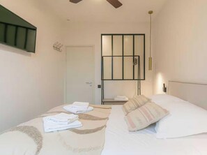 Ein Schlafzimmer mit Bett, Nachttisch, an der Wand montiertem Fernseher und einer Tür.