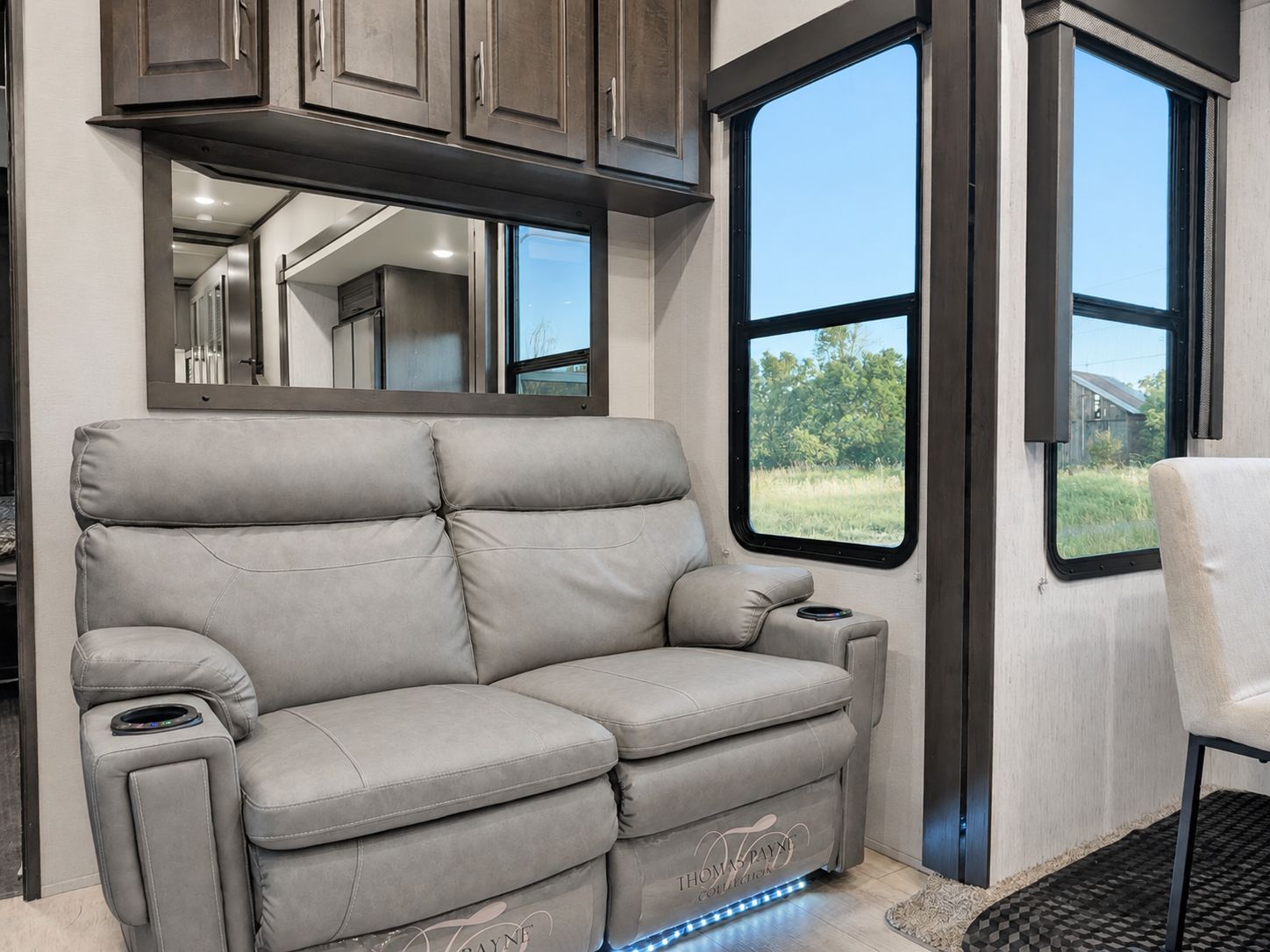 A gray leather sofa with a built-in console table and a remote control, positioned in a room with large windows and a view of greenery.