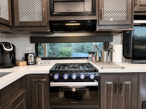 A kitchen with a gas stove, oven, microwave, and a coffee maker.