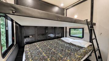 A compact bedroom with a bunk bed, a window with a view, and a ladder.