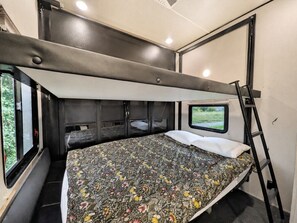 A compact bedroom with a bunk bed, a window with a view, and a ladder.