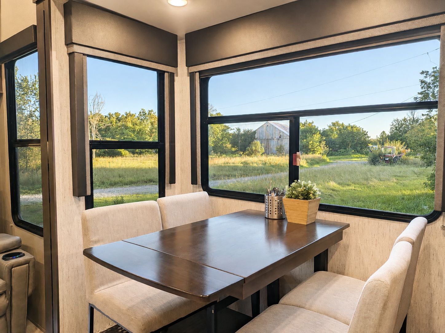 Ein modernes Wohnmobil-Interieur mit Esstisch und Sitzgelegenheiten, große Fenster mit Blick auf eine ländliche Landschaft.