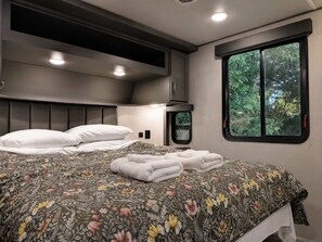 Una camera da letto con un letto, cuscini, una finestra vista verde e una testiera con illuminazione integrata.