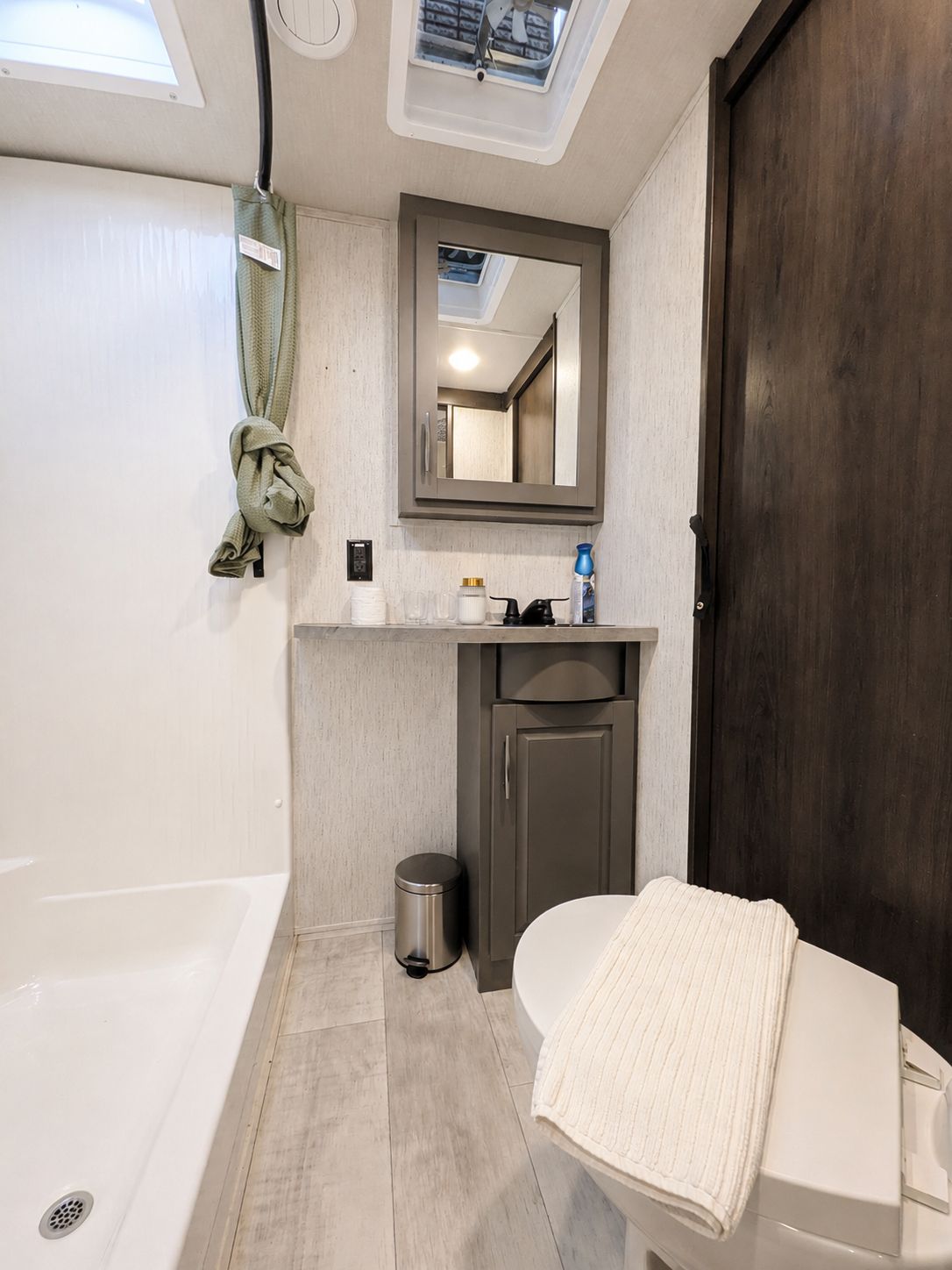 Ein kleines Badezimmer mit Dachfenster, einem Handtuch auf der Toilette, einem Mülleimer und einem Spiegel über dem Waschbecken.