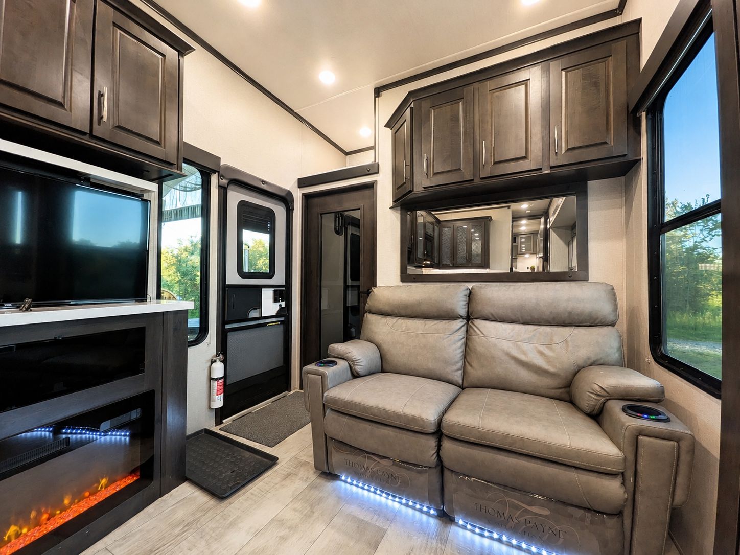 A modern RV interior with a flat-screen TV, a fireplace, a sofa, and a kitchen area.