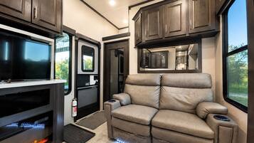 A modern RV interior with a flat-screen TV, a fireplace, a sofa, and a kitchen area.