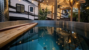 Una piscina con un pontile in legno, circondata da una zona esterna coperta con luci a tendina.
