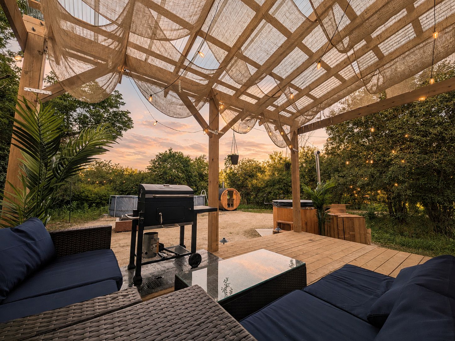 Eine Terrasse im Freien mit einer Pergola, einer Sitzgelegenheit, einem Grill und einem Holztisch.