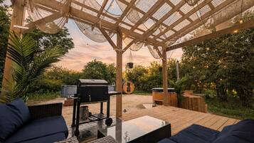Eine Terrasse im Freien mit einer Pergola, einer Sitzgelegenheit, einem Grill und einem Holztisch.