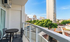 A balcony with a table and chairs, overlooking a cityscape with tall buildings and greenery. - Studio w/ Balcony in Condo. w/ Pool Msu0305 (Governador Valadares)