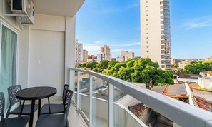 A balcony with a table and chairs, overlooking a cityscape with tall buildings and green trees. - Studio w/ Balcony in Condo. w/ Pool Msu0305 (Governador Valadares)