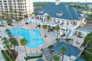 Ein Resort mit einem großen Schwimmbecken, mehreren Liegebereichen und einem mehrstöckigen Gebäude mit Balkonen.