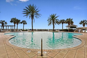 Ein kreisförmiger Pool mit Palmen und Liegestühlen, umgeben von einer gefliesten Terrasse.