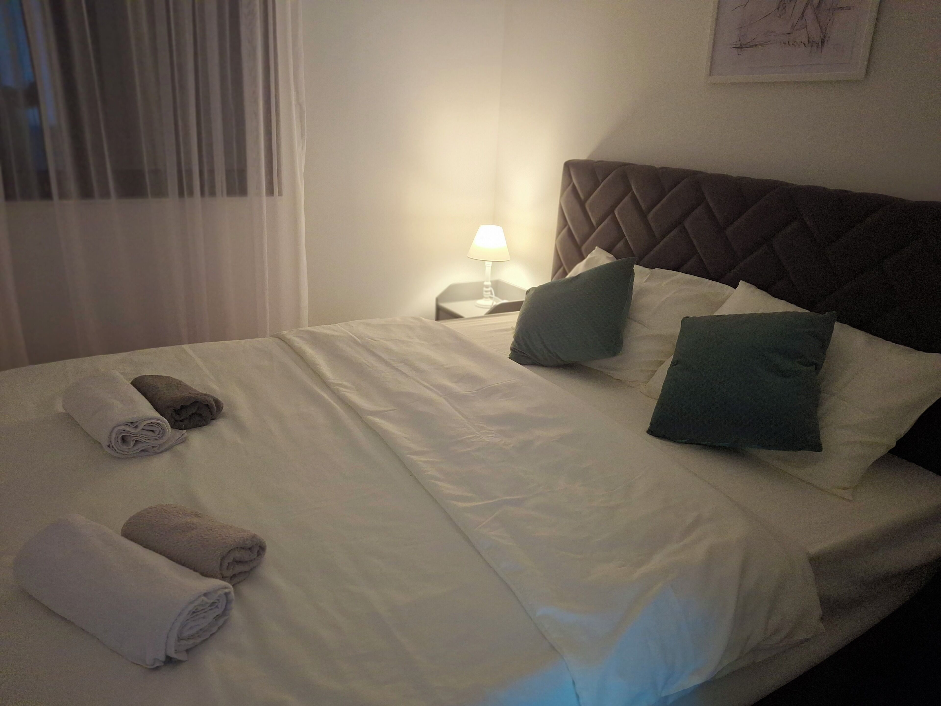 Ein ordentlich bezogenes Bett mit Kissen und zusammengerollten Handtüchern, einer Nachttischlampe und einem Kopfteil.