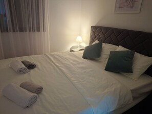 A neatly made bed with pillows and rolled towels, a bedside lamp, and a headboard. - Cozy 1-bedroom apartment in fantastic Kotor with AC (Kotor)
