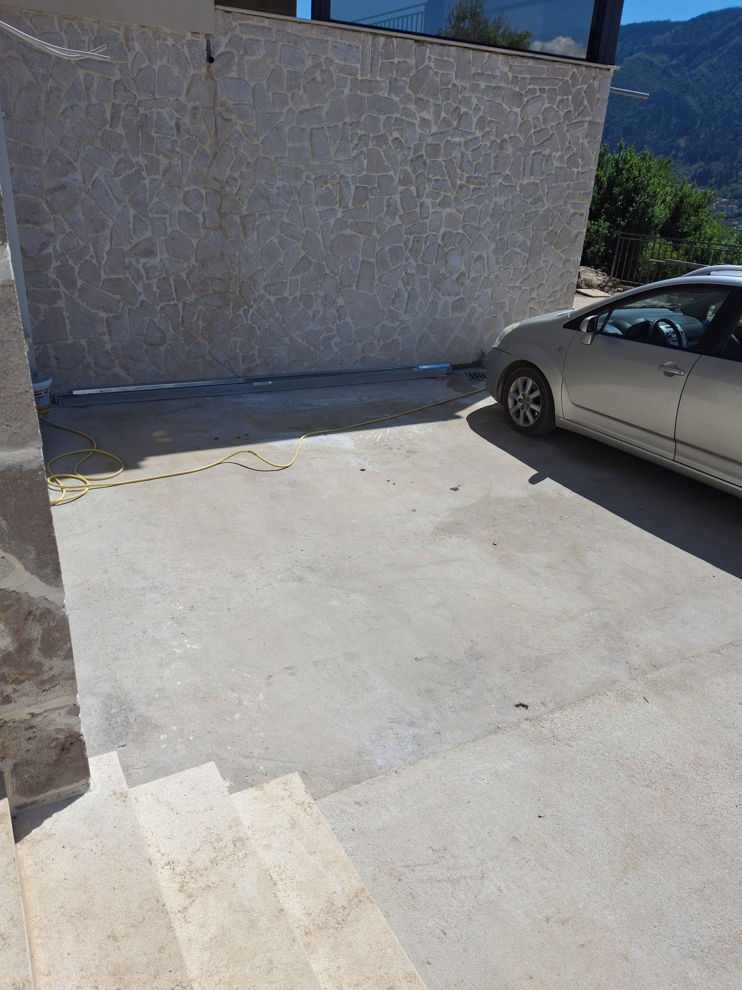 A car parked in a driveway with a stone wall and a clear view of the surrounding landscape.
