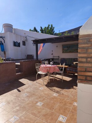 Eine Terrasse im Freien mit Tisch, Stühlen, einem Grill und einem Wandgemälde.