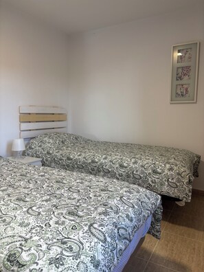 Ein Schlafzimmer mit zwei Betten, einem Nachttisch mit Lampe und einem an der Wand hängenden Kunstwerk.