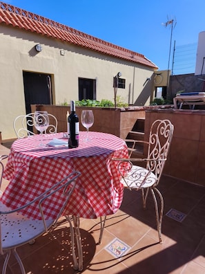 Eine Terrasse im Freien mit einer karierten Tischdecke, Metallstühlen, einer Weinflasche und einem Glas.