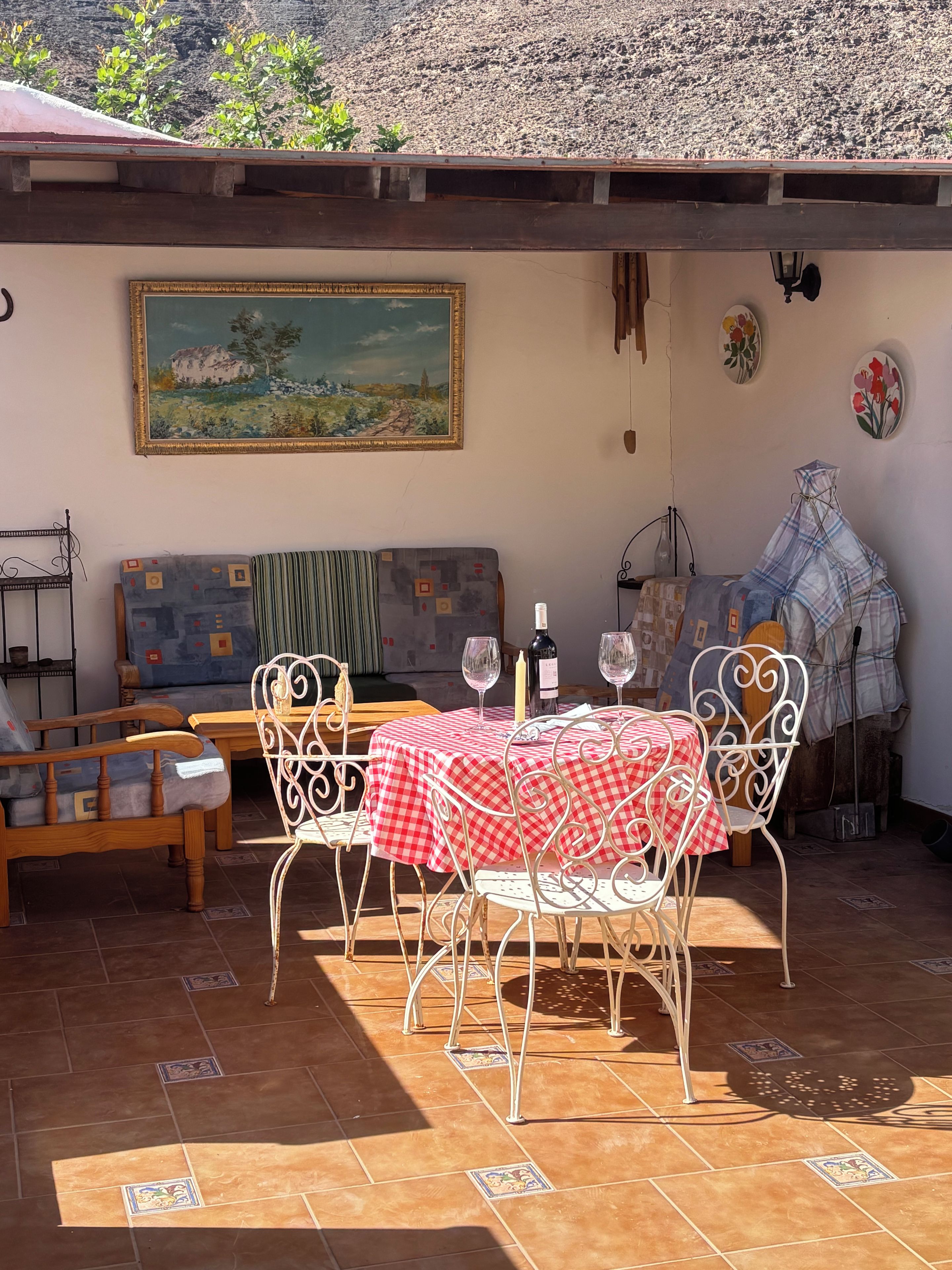 A patio with a table set for two, a sofa, and a painting on the wall.