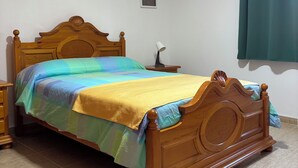 A bedroom with a wooden bed, a bedside table, a lamp, and a wall-mounted picture. - STAR OF THE SOUTH (Valle La Lajita)