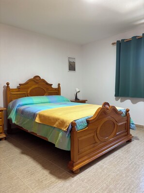 Une chambre à coucher avec un lit en bois, une table de chevet, une lampe et un tableau accroché au mur.