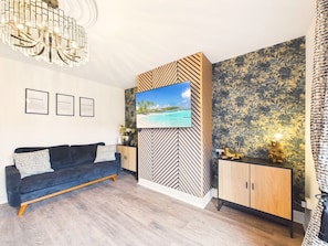 Un soggiorno moderno con un divano, una TV montata su una parete decorata e un mobiletto in legno.