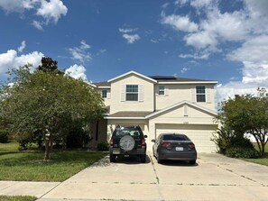 A two-story house with a garage, two cars parked in front, and a clear sky. - CLOSE TO DISNEY 45 m. Cozy 3bed 3bath house in Apopka w fitness room-pool! (Apopka)