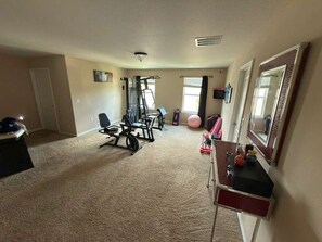 A home gym with exercise equipment, a large mirror, and a carpeted floor. - CLOSE TO DISNEY 45 m. Cozy 3bed 3bath house in Apopka w fitness room-pool! (Apopka)