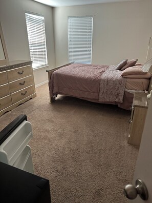 Een slaapkamer met een bed, een dressoir en twee ramen.
