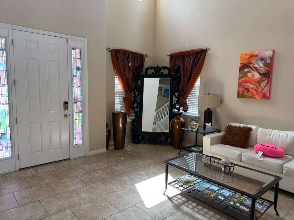 A living room with a white sofa, a glass coffee table, a mirror, and a painting on the wall.