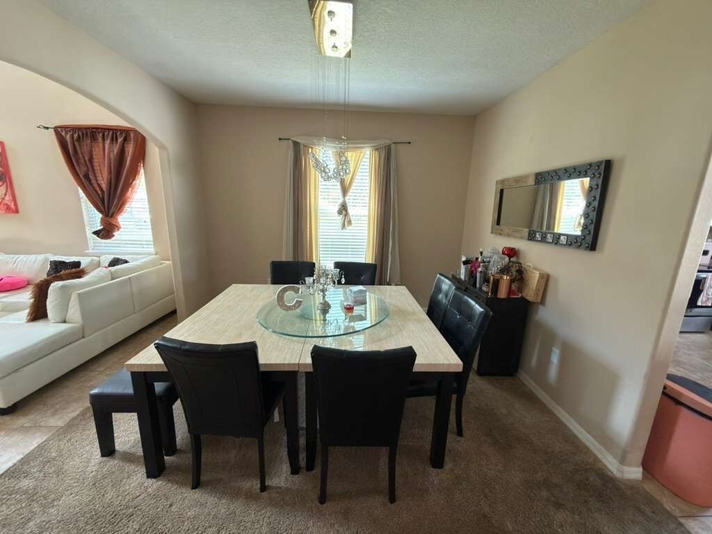 Un coin repas avec une table à plateau en verre, des chaises noires, un canapé blanc et un miroir au mur.