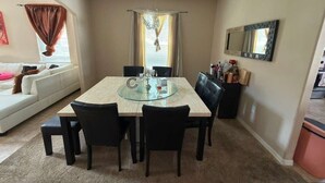 A dining area with a glass-top table, black chairs, a white sofa, and a mirror on the wall. - CLOSE TO DISNEY Cozy 3 bed/3 bed house in tranquil Apopka w fitness room/ pool (Apopka)