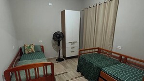 A small, well-lit room with two wooden beds, a wardrobe, a fan, and a window with curtains. - Vrbo Property (Araçariguama)