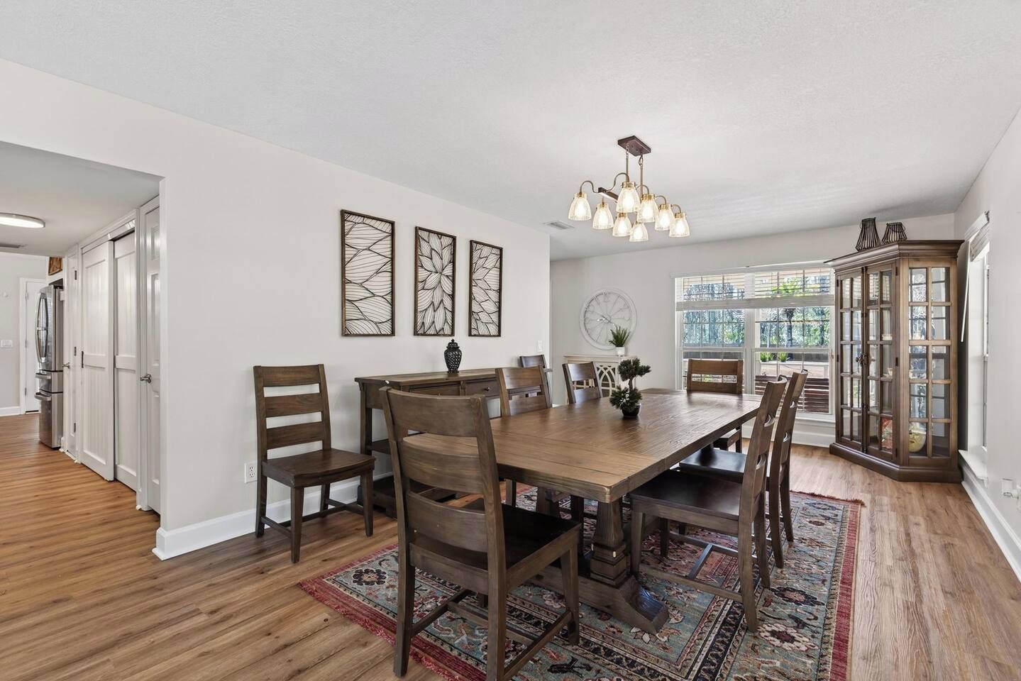 A dining area with a wooden table, chairs, a chandelier, and a patterned rug.