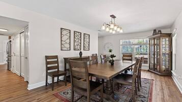 A dining area with a wooden table, chairs, a chandelier, and a patterned rug.