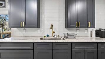 A kitchen with dark cabinets, a white tiled backsplash, a stainless steel sink, and a gold faucet.
