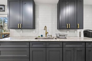 A kitchen with dark cabinets, a white tiled backsplash, a stainless steel sink, and a gold faucet.