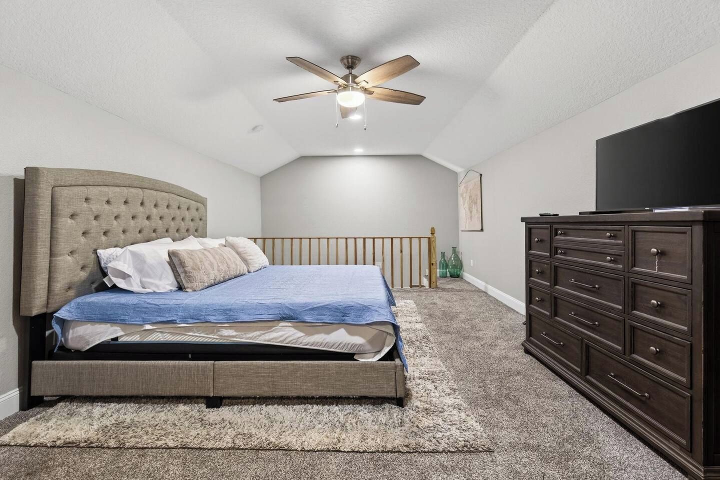 A bedroom with a bed, a dresser, a ceiling fan, and a television.