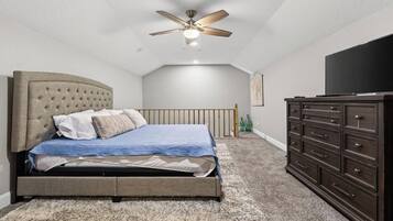 A bedroom with a bed, a dresser, a ceiling fan, and a television.