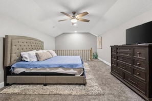 A bedroom with a bed, a dresser, a ceiling fan, and a television.