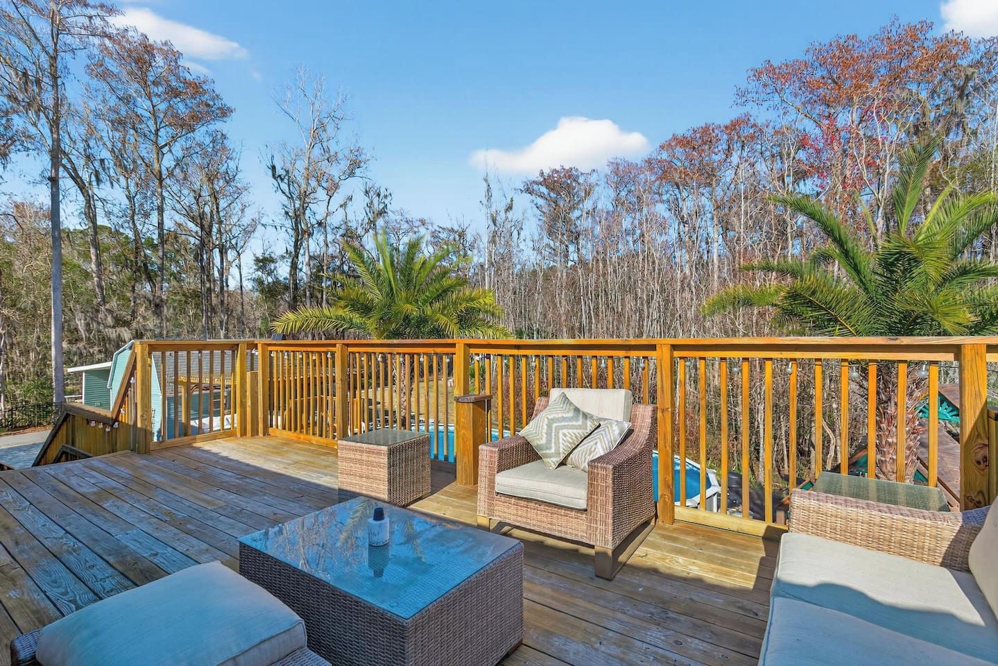 A wooden deck with outdoor furniture, including a sofa and chairs, overlooking a swimming pool.
