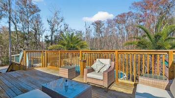 A wooden deck with outdoor furniture, including a sofa and chairs, overlooking a swimming pool.
