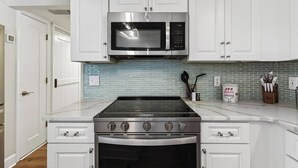 Una cucina con mobili bianchi, un piano cottura in acciaio inossidabile, un forno a microonde e uno schienale piastrellato.