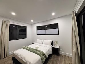 A bedroom with a bed, bedside tables, a window, and a wall-mounted light fixture. - Spacious 5BR Home, Private Pool Near Syd Airport (Bexley)