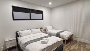 A bedroom with two beds, a nightstand, and a window with blinds. - Spacious 5BR Home, Private Pool Near Syd Airport (Bexley)