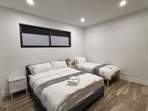 A bedroom with two beds, a nightstand, and a window with blinds. - Spacious 5BR Home, Private Pool Near Syd Airport (Bexley)