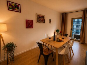 Zona de menjador amb taula de fusta, cadires, una ampolla de vi i un plat de fruita.