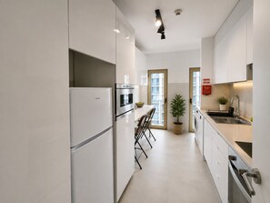 Una cuina moderna amb armaris blancs, forn integrat, nevera i una pica.